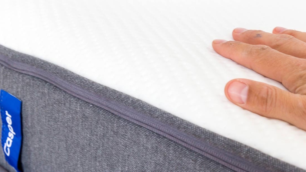 Flat hand lays on white and grey Casper mattress